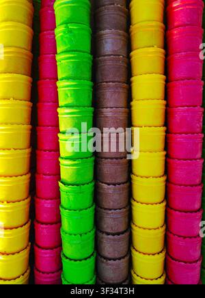 Cones de glace gaufrée brillants empilés en rangées verticales de couleurs. Les cônes jaunes, roses, verts et au chocolat créent un riche motif géométrique et un arrière-plan attrayant. La composition colorée est parfaite pour les desserts d'été, les confiseries, les glaciers, les vacances et les aliments pour bébés Banque D'Images