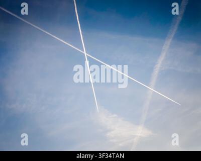 Traînées de condensation d'avion croisant un ciel bleu clair, des traînées de vapeur blanches créant un motif abstrait sur un fond bleu vif, aviation atmosphérique Banque D'Images