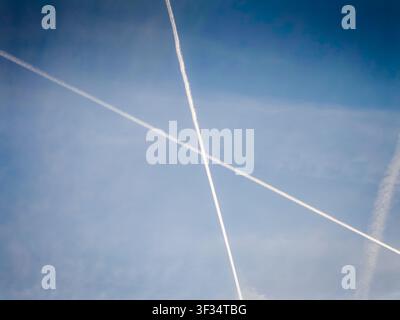 Traînées de condensation d'avion croisant un ciel bleu clair, des traînées de vapeur blanches créant un motif abstrait sur un fond bleu vif, aviation atmosphérique Banque D'Images