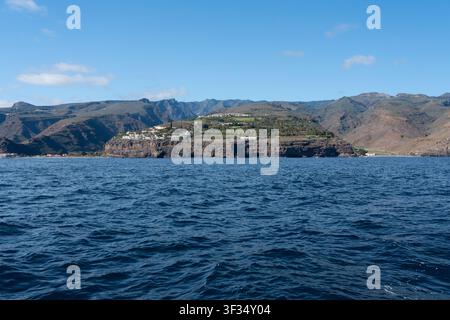 Un village de station balnéaire blanc sur les falaises avec des terrasses vertes sur la côte volcanique accidentée de La Gomera au-dessus de l'océan Atlantique bleu profond, vu depuis la mer, Îles Canaries, Espagne. Banque D'Images