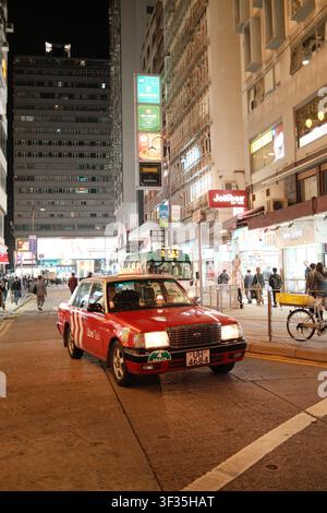 Taxi urbain iconique rouge et blanc roulant dans une rue de la ville, Hong Kong, Chine. Banque D'Images