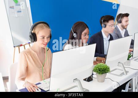 Opérateurs de centres d'appels multiethniques avec micro-casques/oreillettes qui parlent en ligne à des clients au bureau moderne Banque D'Images