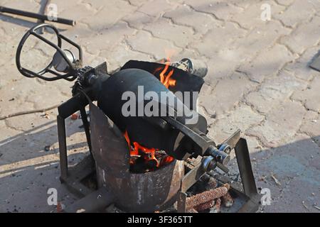 Une machine à popcorn traditionnelle alimentée au charbon en plein air en fonctionnement sur une rue pavée : une bouilloire en fer noir scellée repose sur un feu de charbon ardent, suppor Banque D'Images