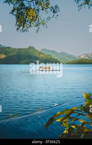 Maison sur radeau d'élevage de poissons flottante sur un lac bleu calme encadré par des feuilles et des montagnes vertes, Hoa Binh, Vietnam Banque D'Images