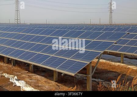 Grand plan d'une centrale solaire photovoltaïque à grande échelle présentant des rangées de panneaux solaires bleus installés sur des supports métalliques, dans un paysage sec et doré Banque D'Images