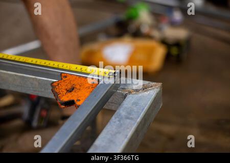 Un cadre métallique de mesure avec mètre ruban et pince à souder sur un tube carré en acier, gros plan montrant les détails de construction et les outils d'atelier Banque D'Images