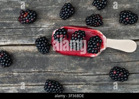Une glace à l’eau repose sur une planche en bois rustique. Des mûres sont éparpillées sur la glace et autour d’elle. C’est l’été et il fait chaud, et la glace est s Banque D'Images