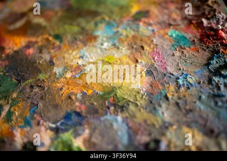 Gros plan de la surface de la palette du peintre avec des peintures à l'huile mélangées séchées et des coups de pinceau texturés dans des tons chauds Banque D'Images