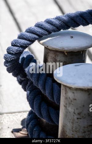Corde tressée bleue enroulée autour d'un bittement en métal dans une marina, illustrant le travail maritime et les responsabilités du quai. Banque D'Images