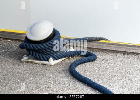 Corde tressée bleue enroulée autour d'un bittement en métal dans une marina, illustrant le travail maritime et les responsabilités du quai. Banque D'Images