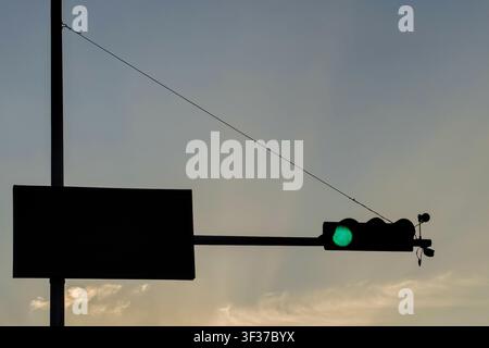 Silhouette d'un feu de circulation vert avec panneau routier vierge contre un ciel nuageux dramatique. Parfait pour les concepts de transport, circulation routière, permission, mouvement, sécurité et urbain. Banque D'Images