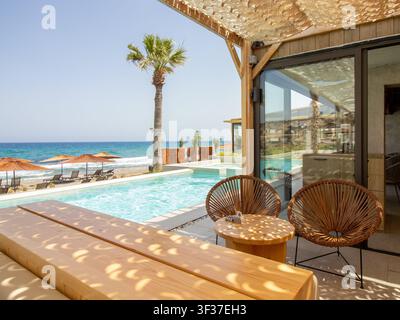 Terrasse de resort de luxe moderne en bord de mer avec chaises tissées rondes, table en bois et piscine privée surplombant la mer Méditerranée Banque D'Images