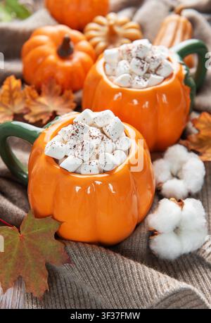 Deux mugs chauffants en forme de citrouille remplis de cacao et de guimauves sur un pull confortable avec un décor d'automne Banque D'Images