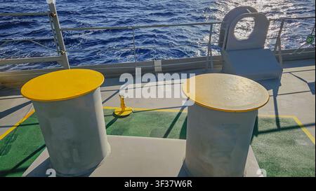 Vue rapprochée de poteaux d'amarrage en métal jaune sur le pont d'un navire avec un fond d'eau bleue de l'océan pour le transport maritime et l'industrie nautique Banque D'Images
