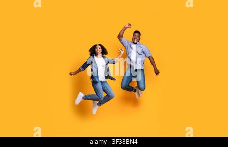 Homme et femme noirs heureux sautant ensemble en studio, expression joyeuse, concept de fitness Banque D'Images