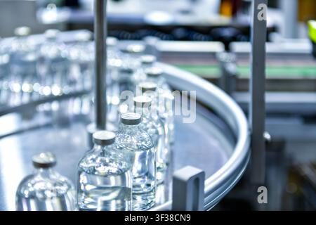 Ligne de production pharmaceutique automatisée remplissant et scellant des flacons en verre de médicaments sur un convoyeur rotatif dans une salle blanche d'usine Banque D'Images