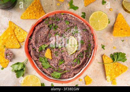 Haricots refrits maison mexicains avec fromage râpé, citron vert, herbes et chips de tortilla nachos. Nourriture de fête saine et végan, plat savoureux riche en protéines fait wi Banque D'Images