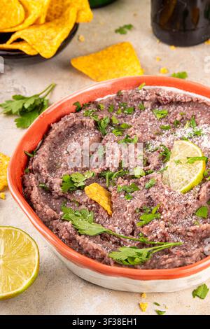 Haricots refrits maison mexicains avec fromage râpé, citron vert, herbes et chips de tortilla nachos. Nourriture de fête saine et végan, plat savoureux riche en protéines fait wi Banque D'Images