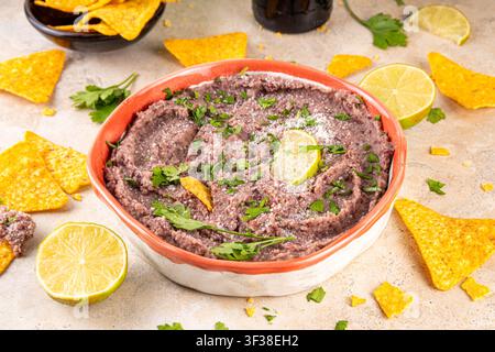 Haricots refrits maison mexicains avec fromage râpé, citron vert, herbes et chips de tortilla nachos. Nourriture de fête saine et végan, plat savoureux riche en protéines fait wi Banque D'Images