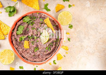 Haricots refrits maison mexicains avec fromage râpé, citron vert, herbes et chips de tortilla nachos. Nourriture de fête saine et végan, plat savoureux riche en protéines fait wi Banque D'Images