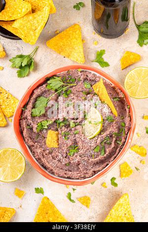 Haricots refrits maison mexicains avec fromage râpé, citron vert, herbes et chips de tortilla nachos. Nourriture de fête saine et végan, plat savoureux riche en protéines fait wi Banque D'Images