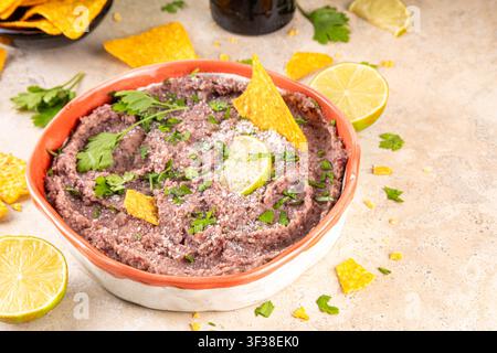 Haricots refrits maison mexicains avec fromage râpé, citron vert, herbes et chips de tortilla nachos. Nourriture de fête saine et végan, plat savoureux riche en protéines fait wi Banque D'Images