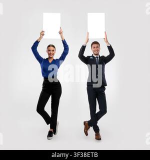 Deux hommes d'affaires tenant un panneau publicitaire blanc vierge au studio Banque D'Images