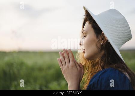 Femme chrétienne priant les yeux fermés dans une prairie de fleurs sauvages au coucher du soleil Banque D'Images