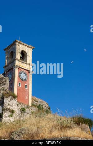 Tour d'horloge historique de la vieille forteresse à Corfou, Grèce, se dressant fièrement sous un ciel bleu clair avec une lune visible Banque D'Images