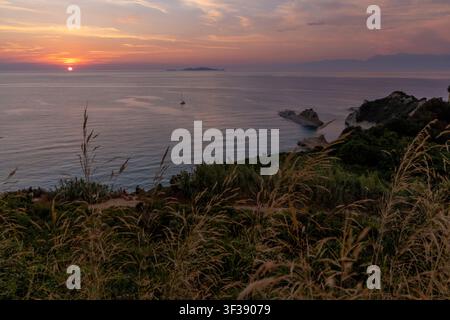 Soleil doré s'éloignant à l'horizon, illuminant les vagues de l'océan près de falaises abruptes et un bateau lointain pendant le crépuscule du soir Banque D'Images