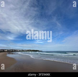 Portrush, en Irlande du Nord, présente une plage de sable s'étendant le long de la côte sous un ciel bleu clair. Des vagues douces déferlent sur le rivage, et un dista Banque D'Images