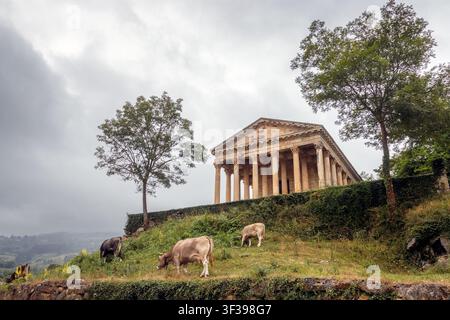 Vue frontale de l'église Saint-Georges, également connue sous le nom de Parthénon de Las Fraguas, en Cantabrie, Espagne, au sommet d'une colline, avec des vaches en train de pâturer Banque D'Images