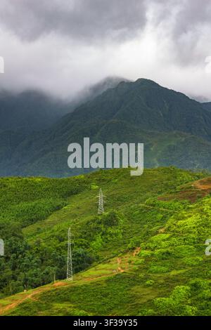 Prise verticale de poteaux électriques s'élevant le long de collines verdoyantes vers des sommets montagneux enveloppés de brouillard à Sapa, province de Lao Cai, dans le nord du Vietnam. Banque D'Images