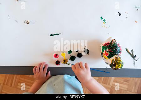 Vue aérienne d'un enfant peignant un jouet dinosaure avec des fournitures artisanales vives Banque D'Images