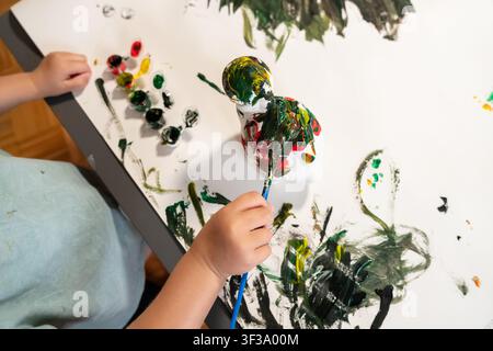Projet de peinture de dinosaure en hauteur avec les mains d'un enfant et des peintures artisanales vives Banque D'Images