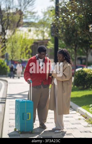 Homme et femme touristes afro-américains concentrés explorant une nouvelle ville, vérifient la carte de l'hôtel sur un smartphone Banque D'Images