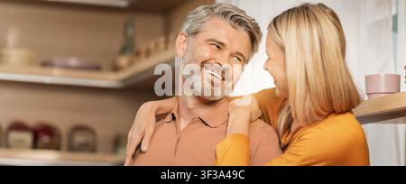 Couple mûr heureux souriant et s'embrassant dans la cuisine, concept d'amour et de connexion Banque D'Images