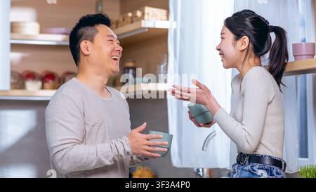 Homme et femme asiatiques heureux riant et discutant dans une cuisine moderne Banque D'Images