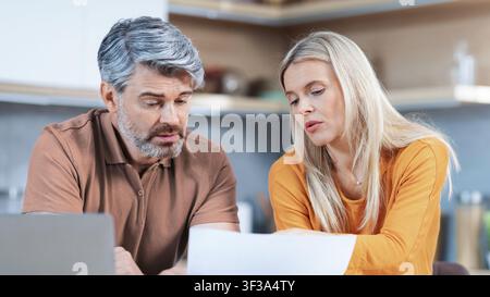 Couple caucasien d'âge moyen concentré examinant des documents à la maison, concept commercial Banque D'Images
