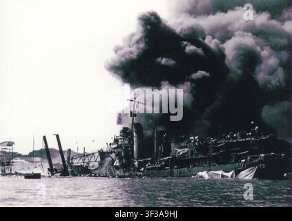 Photographie dramatique capturant l'USS Shaw (DD‑373) quelques instants après l'explosion de ses soutes à munitions avant lors de l'attaque japonaise sur Pearl Harbor le 7 décembre 1941. Le destroyer, positionné dans la cale sèche flottante YFD‑2, est enveloppé d'une colonne imposante de fumée noire tandis que les débris s'éparpillent sur le quai. Le numéro de coque „73“ est visible à la proue, identifiant le navire au moment de ses dommages catastrophiques. Cette image rare prise avec un appareil photo personnel a été prise par un marin de la marine américaine pendant l'attaque et est restée non développée pendant des décennies avant d'être découverte dans un placard à chaussures au début des années 2000. Banque D'Images