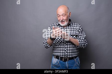 Homme senior joyeux tapant un message sur un smartphone Banque D'Images