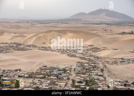 Vue élevée d'une ville du désert, avec des maisons et des bâtiments entourés de vastes dunes de sable et de montagnes Banque D'Images