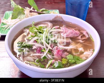Un bol de soupe de nouilles pho vietnamienne avec du bœuf tranché, des herbes fraîches, des germes de haricots et des oignons, servi dans un restaurant vietnamien. Banque D'Images