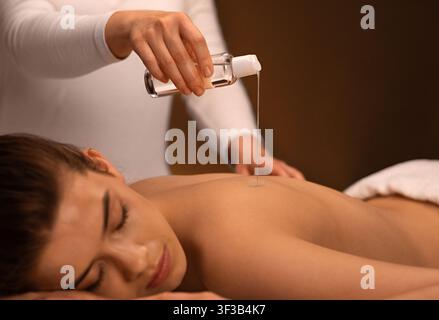 Gros plan de la masseuse verser de l'huile sur le dos de la femme endormi Banque D'Images