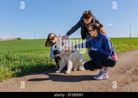 Trois amis souriants caressant un chien de Maremme lors d'une promenade à la campagne Banque D'Images