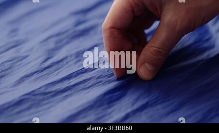 main d'homme vérifiant le tissu synthétique bleu d'un sac Banque D'Images
