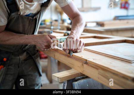 Charpentier professionnel rénovant une porte en bois vintage sur son lieu de travail dans un atelier de restauration Banque D'Images