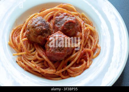 Vue aérienne à angle élevé de spaghettis avec sauce tomate et trois boulettes de viande dans un bol blanc à large bord posé sur une surface sombre Banque D'Images