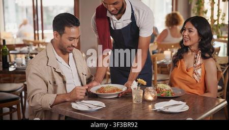 Serveur servant et couple au restaurant pour un rendez-vous, une connexion ou un lien ensemble le week-end. Heureux, nourriture et serveur avec homme et femme pour le dîner Banque D'Images