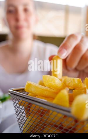 Femme prenant une frite dorée d'un panier en métal avec un fond flou Banque D'Images
